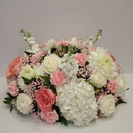 Low centerpiece of white hydrangeas, roses, and pink carnations in a soft pastel palette