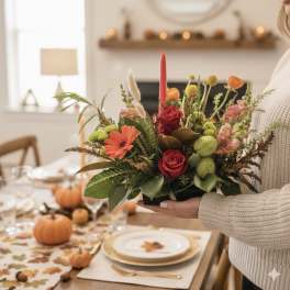 Autumn floral centerpiece with red roses and orange blooms in a low container