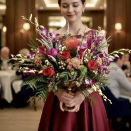 Woman holding a large bouquet of red, pink, and purple flowers in a gold vase