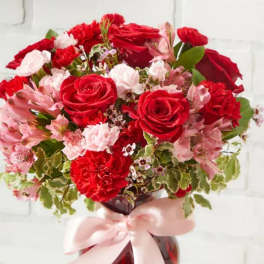 Red roses and pink flowers in a vase with a pink ribbon
