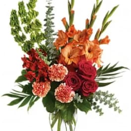 Tall bouquet of orange lilies, red roses, and carnations in a clear vase