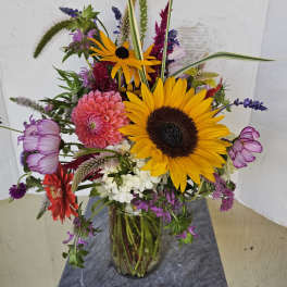 Mixed bouquet with sunflowers, pink blooms, and purple flowers in a glass vase