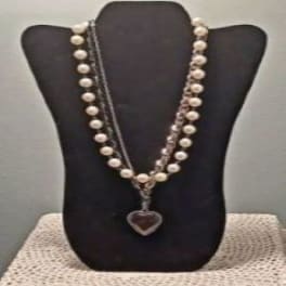 Two pearl necklaces on a black display bust with a heart pendant