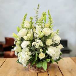 White floral arrangement in a wicker basket with lilies and roses