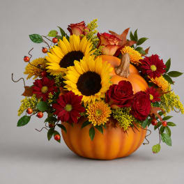 Autumn floral arrangement in a pumpkin container with sunflowers, roses, and mums