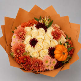 Bouquet of cream roses, orange chrysanthemums, and a small pumpkin wrapped in orange paper