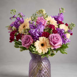 Purple and pink bouquet with cream daisies in a textured glass vase