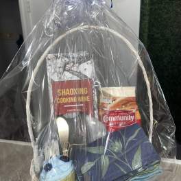 Gift basket with cooking wine, coffee, folded napkins, and a cupcake