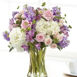 Bouquet of pink roses, white hydrangeas, and purple flowers in a glass vase