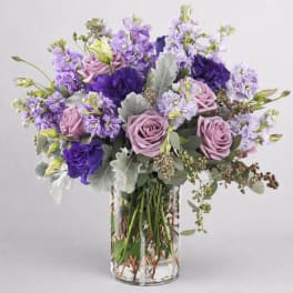 Purple and lavender bouquet of roses and mixed blooms in a clear glass vase