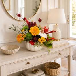 Colorful floral arrangement in a white pumpkin vase on a console table