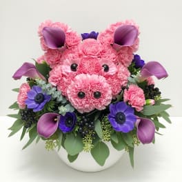 Pink carnation pig arrangement with purple calla lilies and flowers in a white bowl