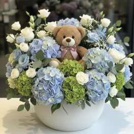 Teddy bear surrounded by blue and white flowers in a white bowl