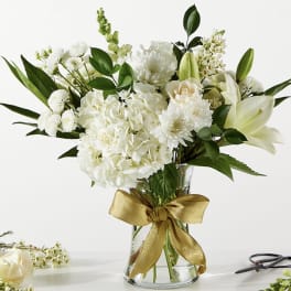 White floral bouquet in a clear glass vase with a gold ribbon