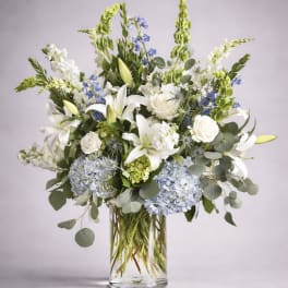 White lilies and blue flowers in a clear glass vase