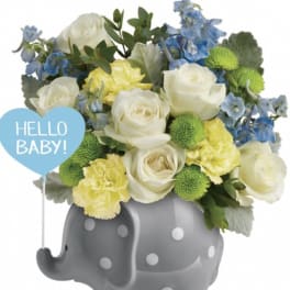 White and blue flowers in a gray polka-dot elephant container with a "Hello Baby!" sign