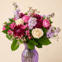 Pink and cream roses with purple blooms in a purple glass vase
