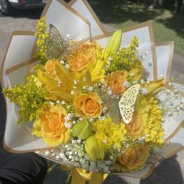 Yellow bouquet with roses, lilies, and daisies wrapped in white paper