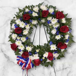 Heart-shaped floral wreath with red roses, white daisies, and blue accents