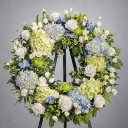 Large floral wreath with white roses, blue hydrangeas, and green blooms