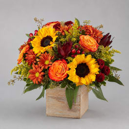 Autumn bouquet with sunflowers, orange roses, and mums in a wooden cube vase