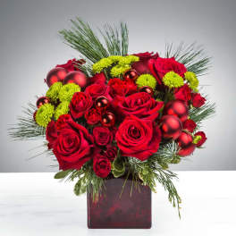 Red roses and green button flowers with red ornaments in a red cube vase