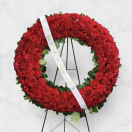 Red floral wreath on a black stand with a white ribbon