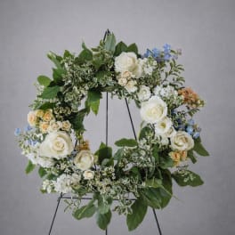Floral wreath with white roses, blue flowers, and greenery on a stand
