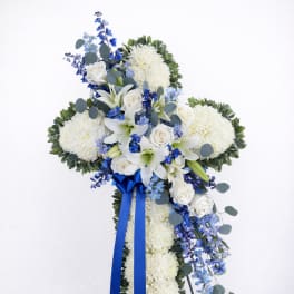 Standing floral cross with white blooms, blue flowers, and a blue ribbon