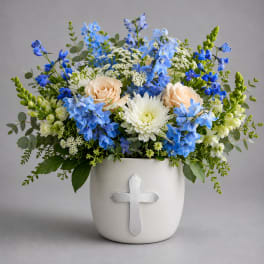 Blue and white floral arrangement in a white vase with a cross emblem