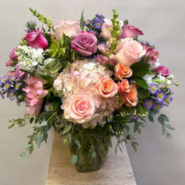 Mixed bouquet of pink roses, hydrangea, and purple daisies in a glass vase