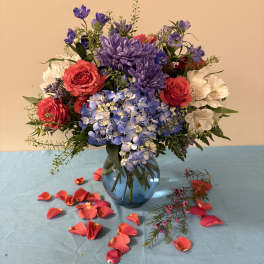 Bouquet of red roses, blue hydrangeas, and purple flowers in a glass vase
