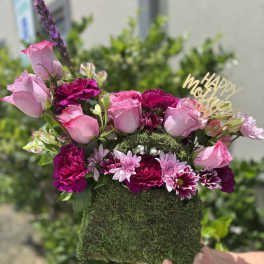 Pink roses and magenta flowers in a moss-covered box with a gold "Happy Mother's Day" topper