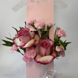 Pink roses and carnations arranged in a pink gift bag with ribbon and butterfly accents.