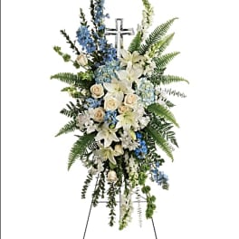 Standing floral spray with white lilies, blue flowers, and a cross
