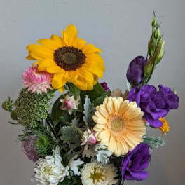 Mixed bouquet with sunflowers, purple blooms, and daisies in a glass vase