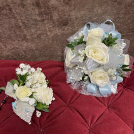 Two white rose bouquets with blue ribbon accents on a red cushion