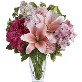 Pink lilies and mixed blooms arranged in a clear glass vase