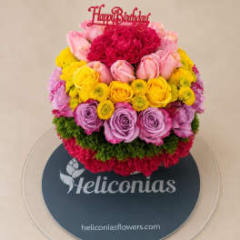 Round bouquet of pink, yellow, and lavender flowers with a Happy Birthday topper