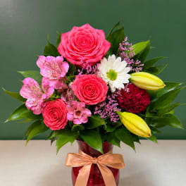 Pink roses and lilies arranged in a red vase with a ribbon