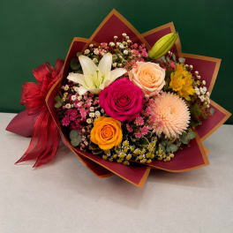 Mixed bouquet with roses, lilies, and a chrysanthemum wrapped in burgundy paper