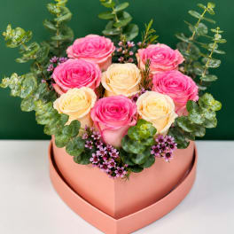 Pink and cream roses arranged in a heart-shaped box