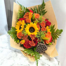 Bouquet of sunflowers, roses, and orange blooms wrapped in kraft paper