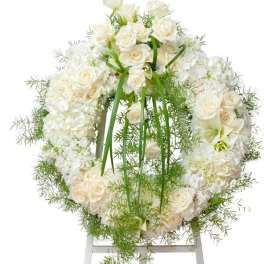 White rose and hydrangea wreath with green ribbon on a stand