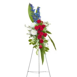 Standing floral spray with red roses, white blooms, and blue flowers on a metal easel