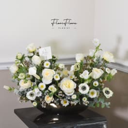 White floral arrangement in a black bowl vase with roses and daisies
