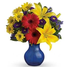 Bouquet of yellow lilies, red gerbera daisies, and purple flowers in a blue vase