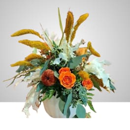Orange roses in a white vase with yellow dried grasses and mixed foliage