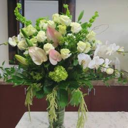 Large white and pale pink floral arrangement in a green glass vase