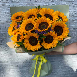 Bouquet of bright yellow sunflowers wrapped in green paper with a yellow ribbon